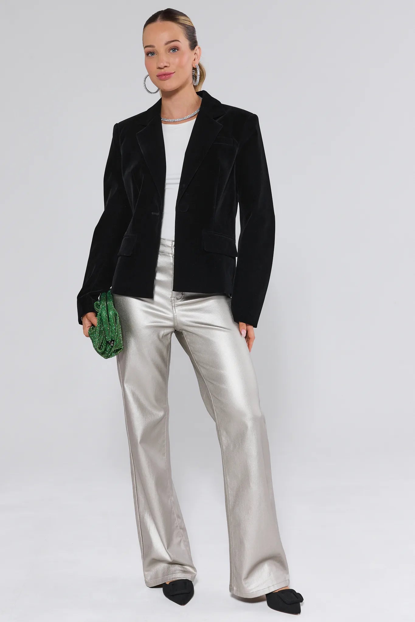 Woman wearing a black blazer, white top, silver pants, and black shoes on a white background