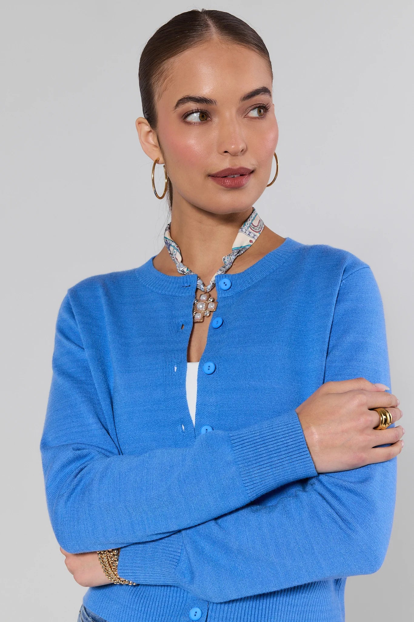 Woman wearing a Sarah Blue Button Up Cardigan and cross necklace with a plain background