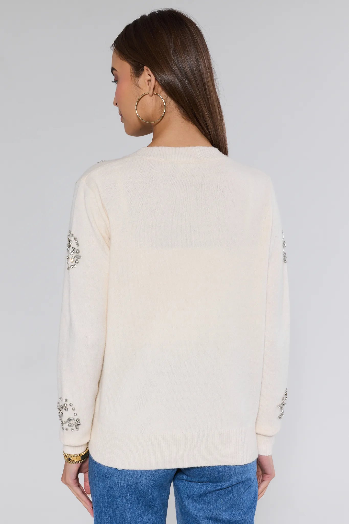 Woman wearing a cream sweater with floral patterns on long sleeves against a plain background