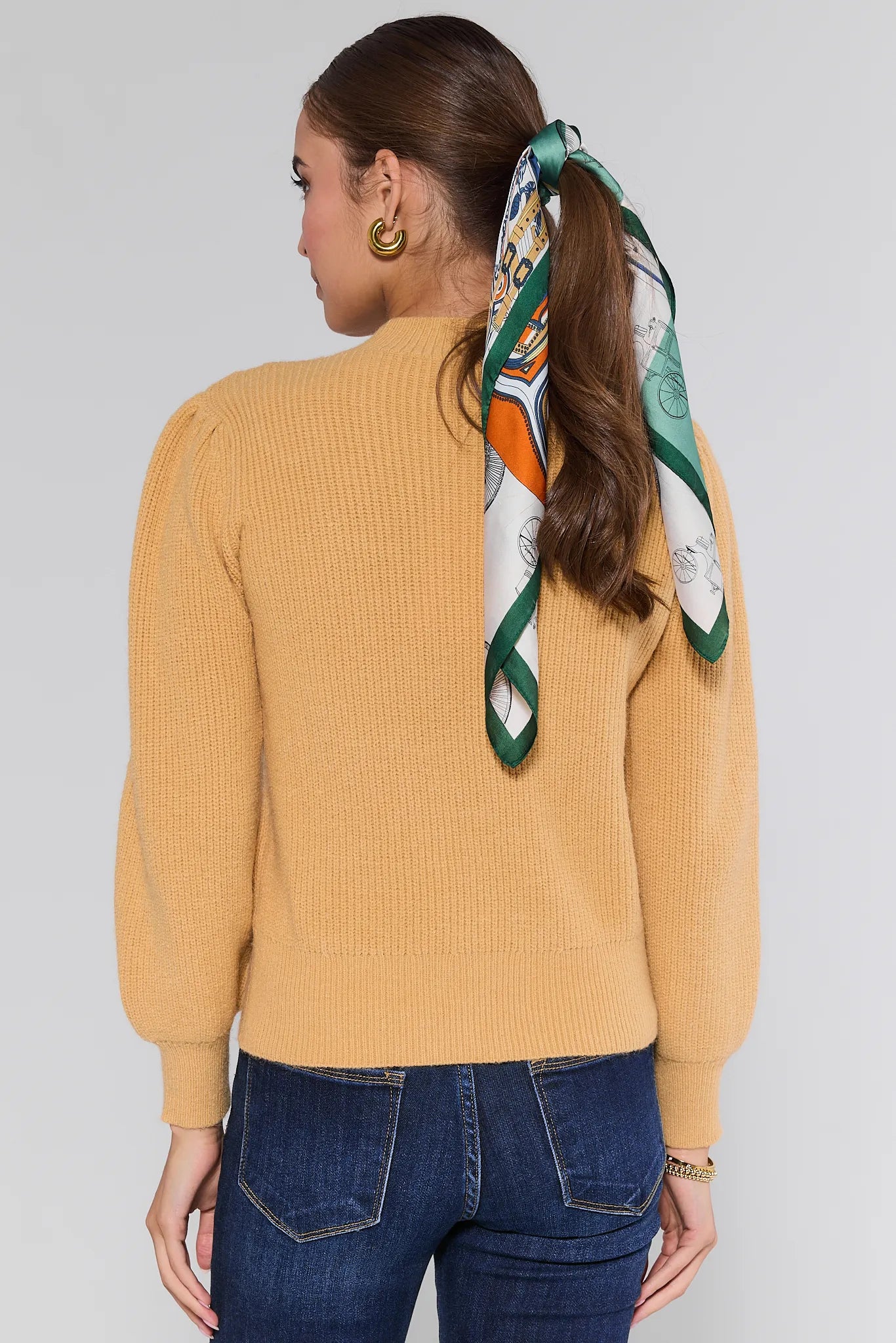 Woman wearing a yellow Dixie Sweater and blue jeans with a green patterned scarf around her neck against a gray background