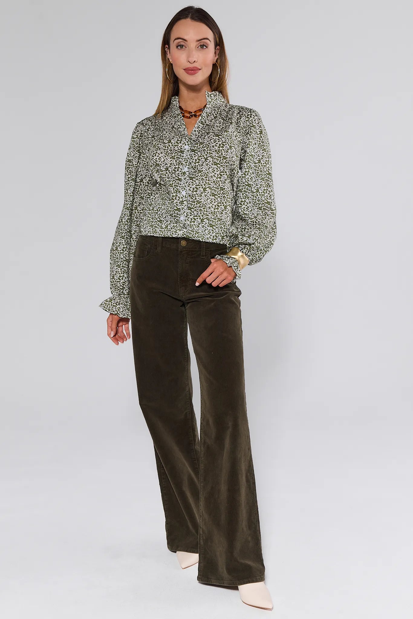 Woman wearing a patterned Mitzi Top and dark green pants on a white background