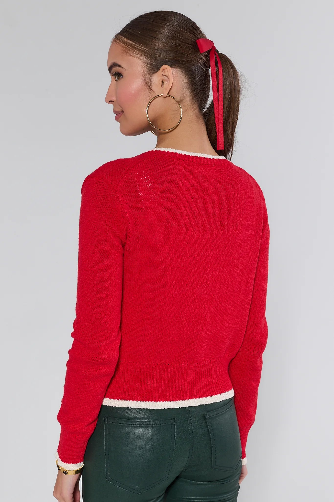 Woman wearing a red Karlie cardigan over a white top and green pants on a plain background