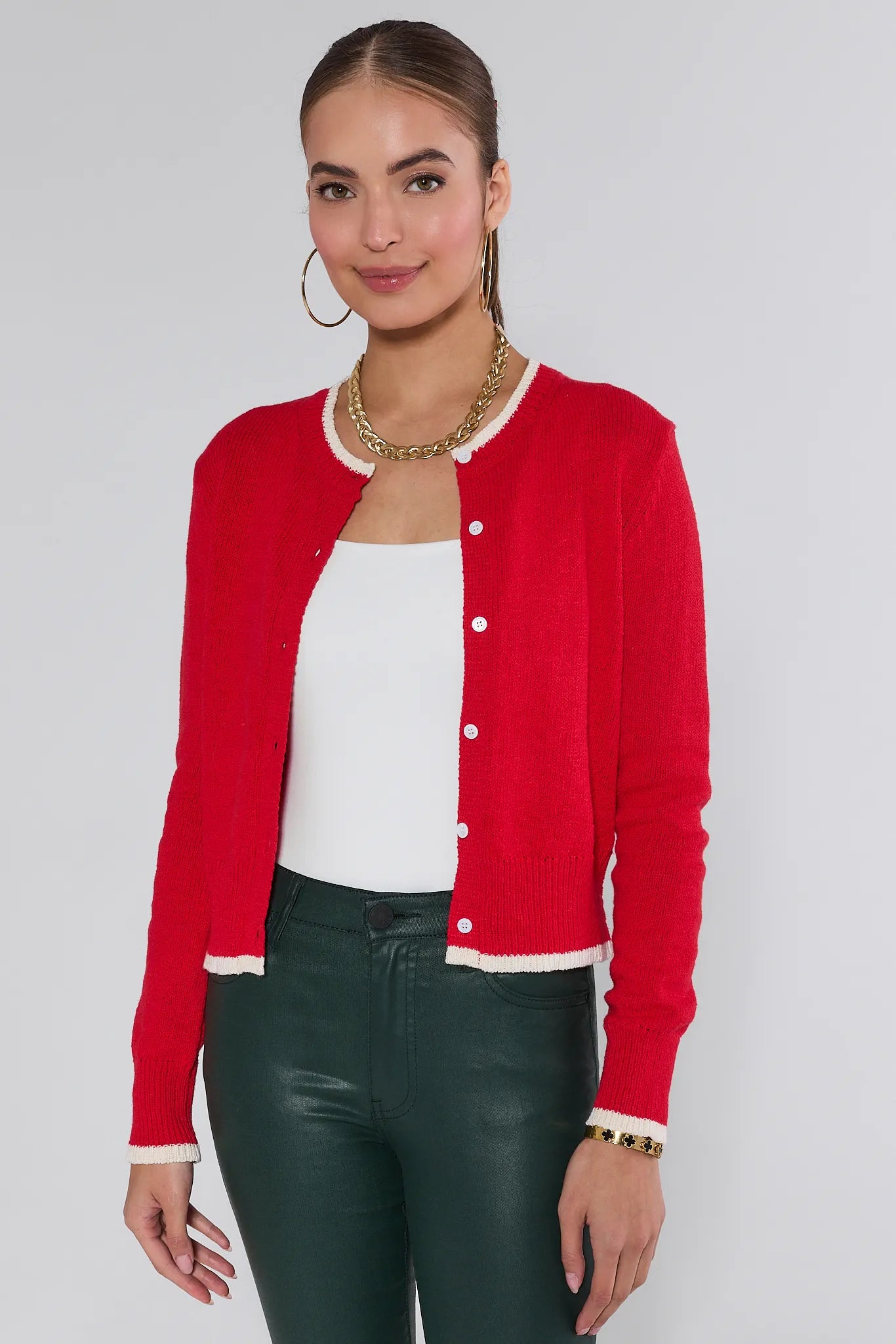 Woman wearing a red Karlie cardigan over a white top and green pants on a plain background