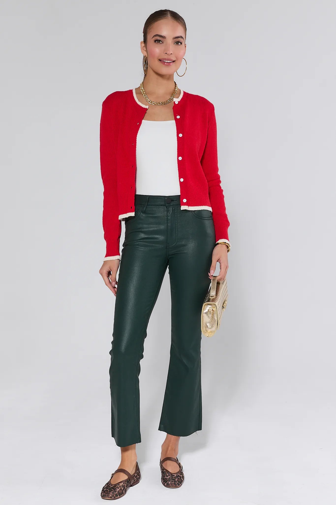 Woman wearing a red Karlie cardigan over a white top and green pants on a plain background