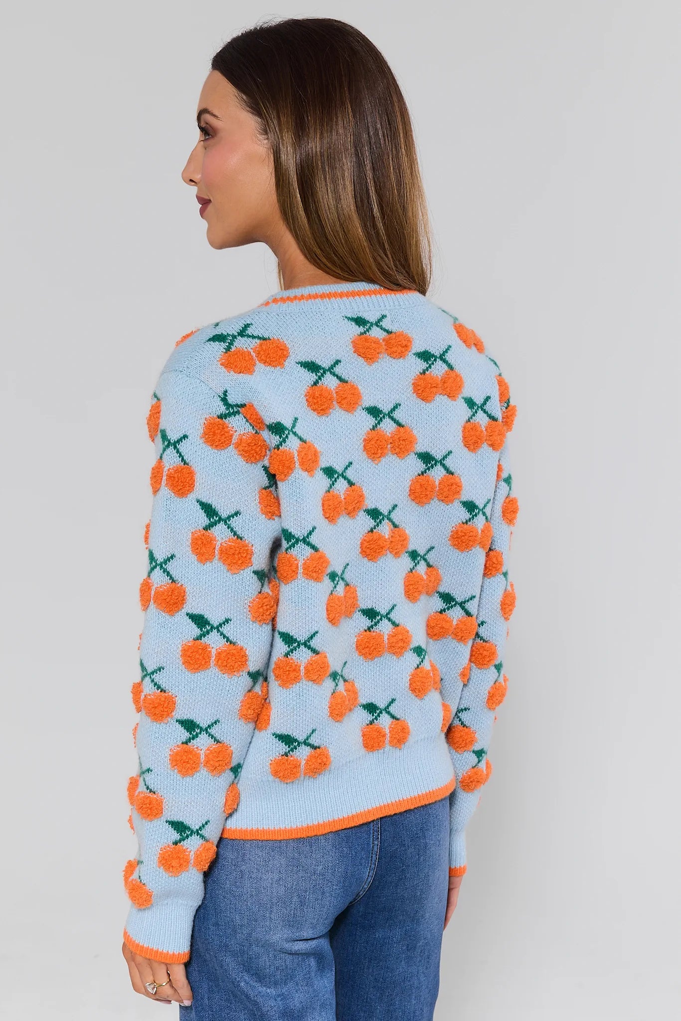 Woman wearing a sweater with orange cherry pattern on a plain background