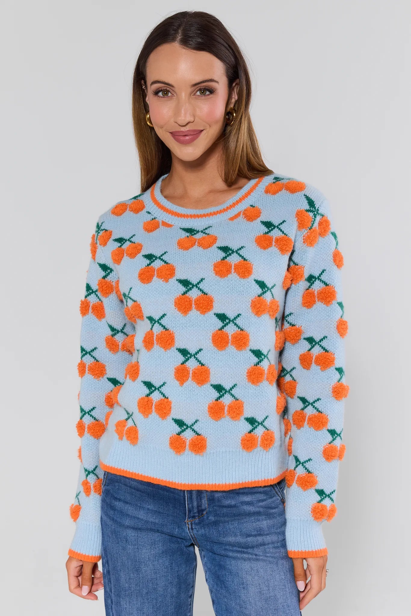 Woman wearing a sweater with orange cherry pattern on a light blue background