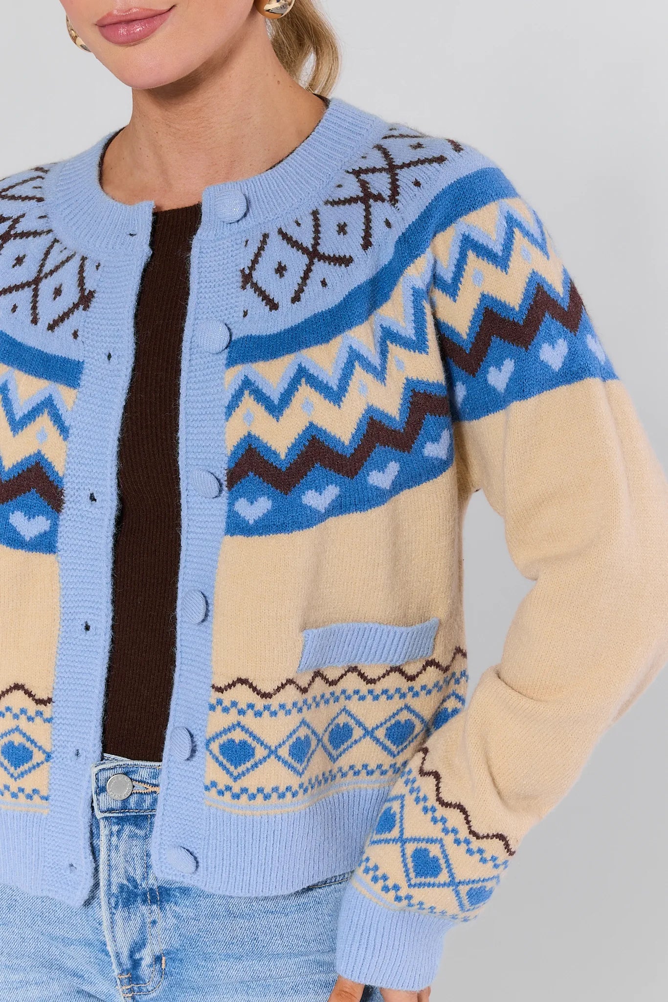 Person wearing a patterned cardigan with blue, beige, and brown colors on a plain background