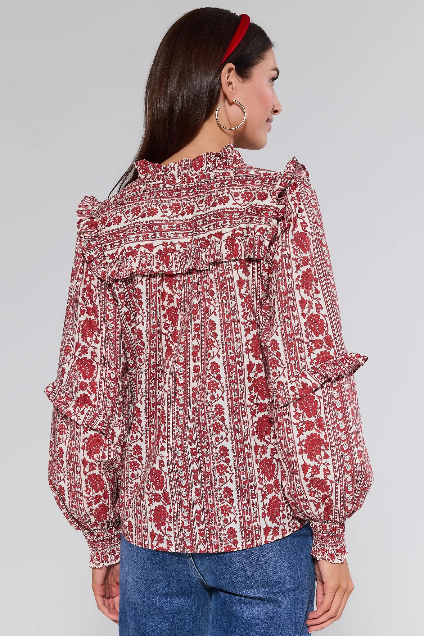 Woman wearing a red and white patterned Morgan Top with blue jeans on a gray background