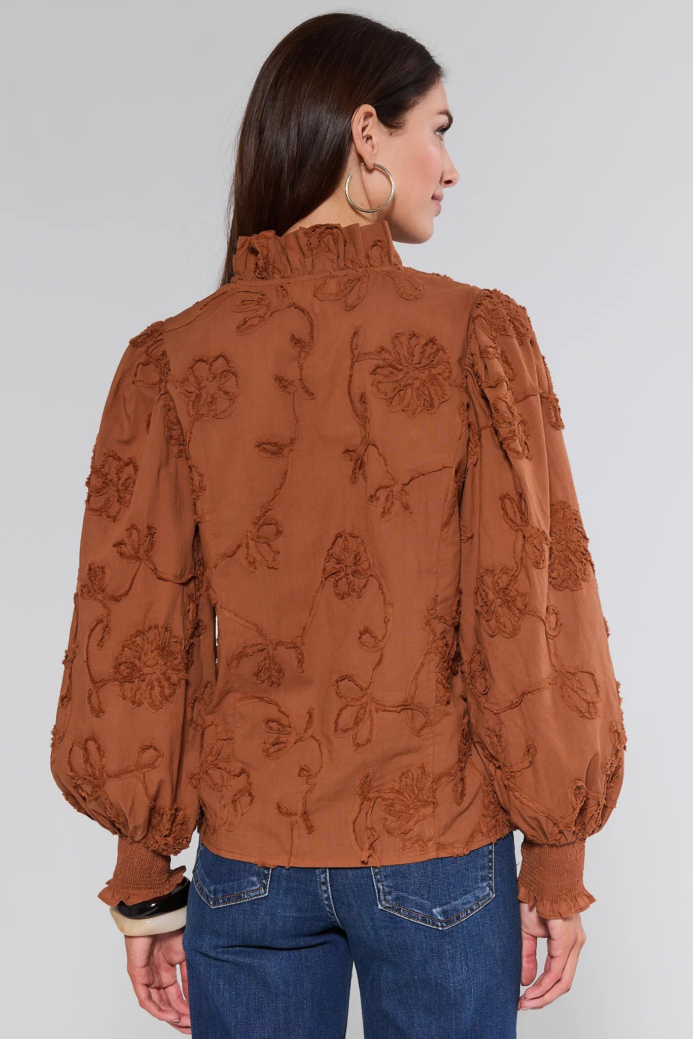 Woman wearing a brown embroidered Shaunda Top with blue jeans on a white background