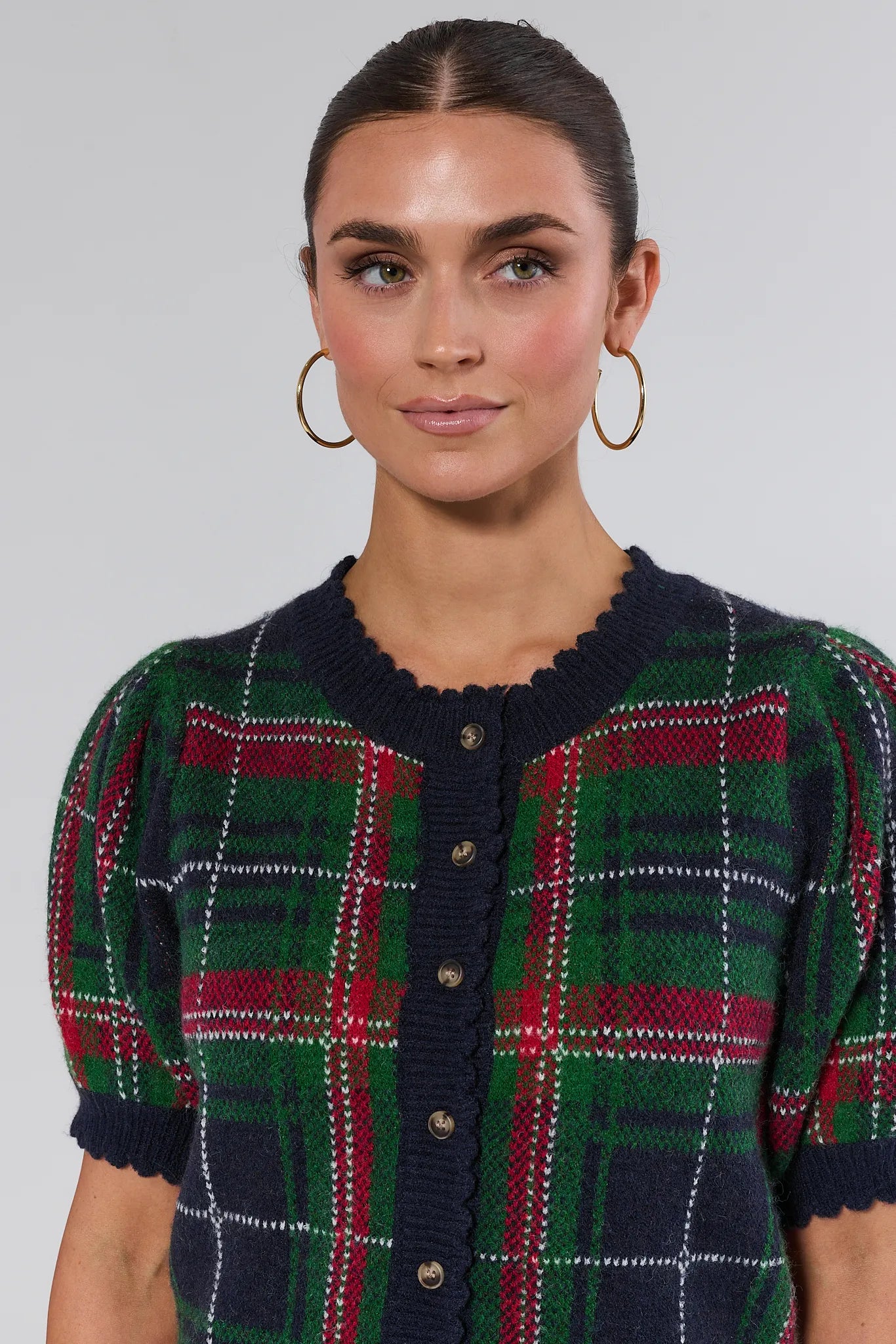 Woman wearing a plaid dress with a green, red, and navy pattern on a plain background
