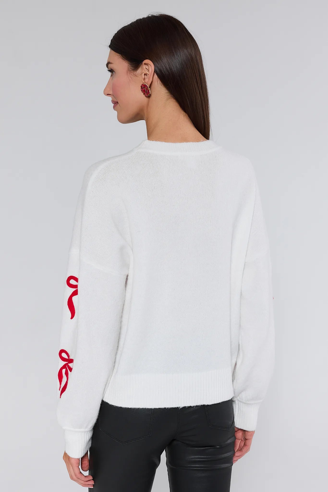 Woman wearing a white sweatshirt with red designs on sleeves against a plain background