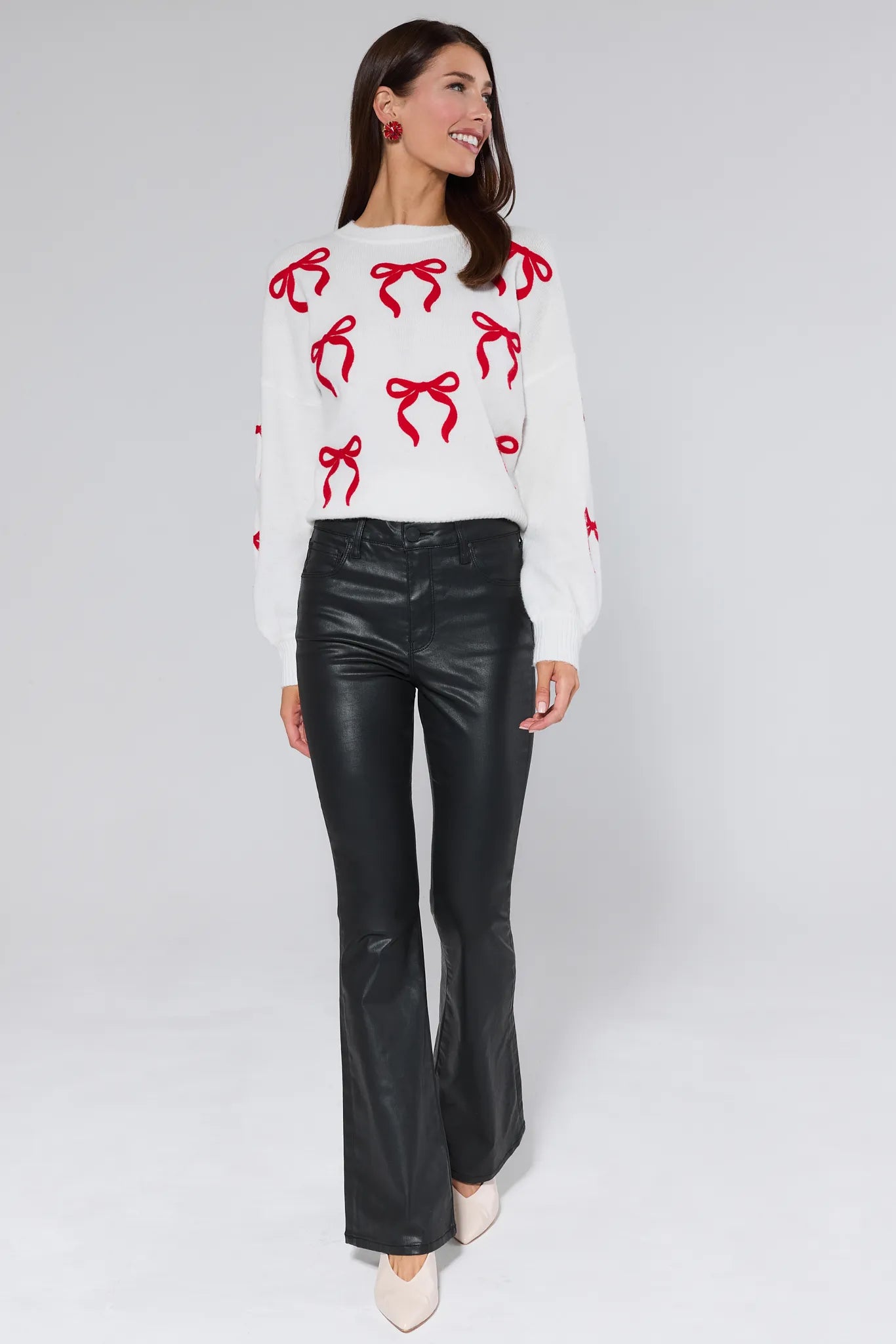 Woman wearing a white sweater with red bow patterns and black leather pants on a white background