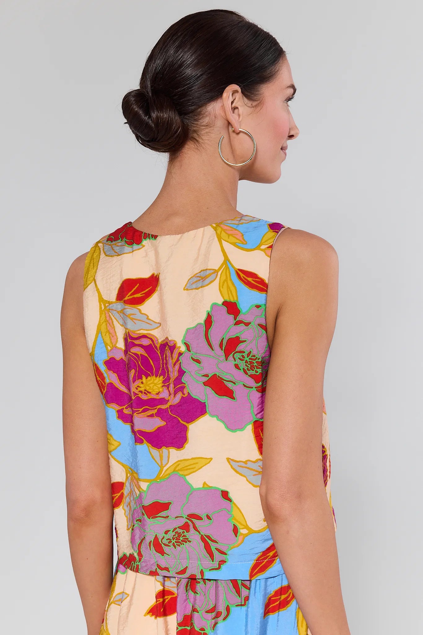 Woman wearing aMarisol Multicolor Floral Tank Top and gold earrings with a plain background