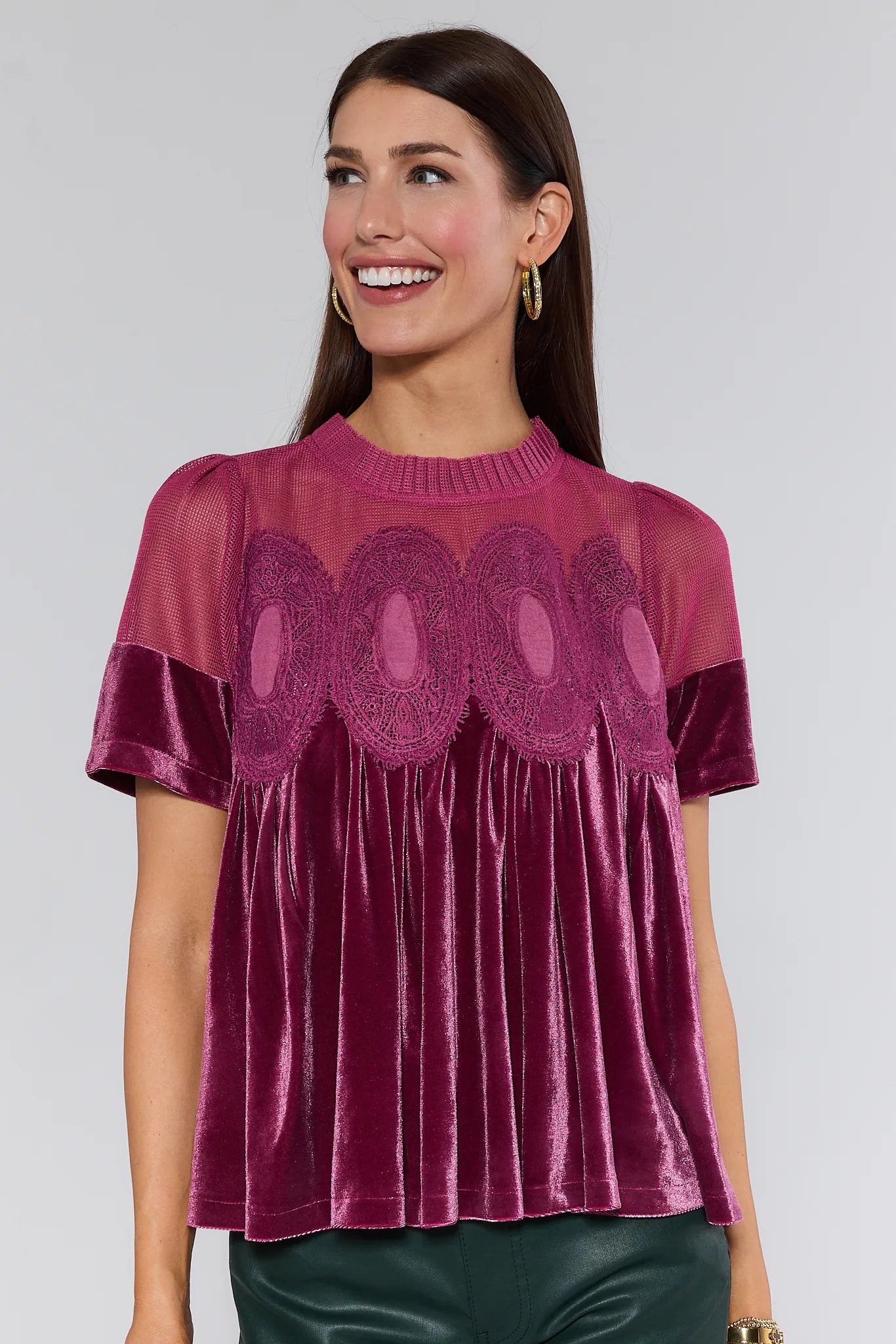Woman wearing a burgundy gabrielle velvet top with lace details on a plain background