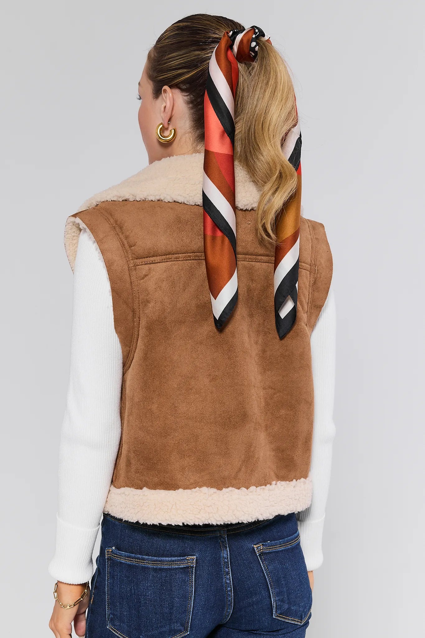 Person wearing a brown suede Whitney Vest with a colorful scarf on a plain background