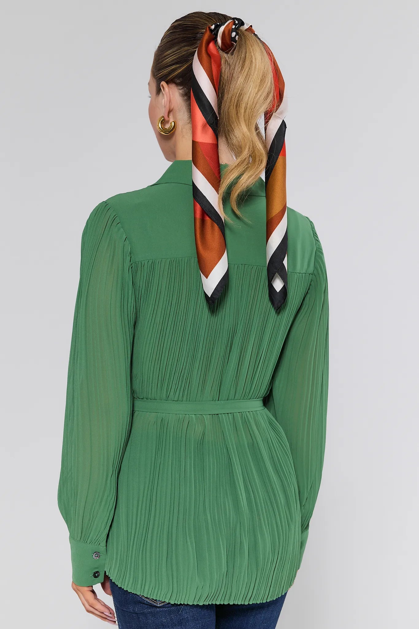 Person wearing a green pleated Miley Top with a colorful scarf in their hair on a white background