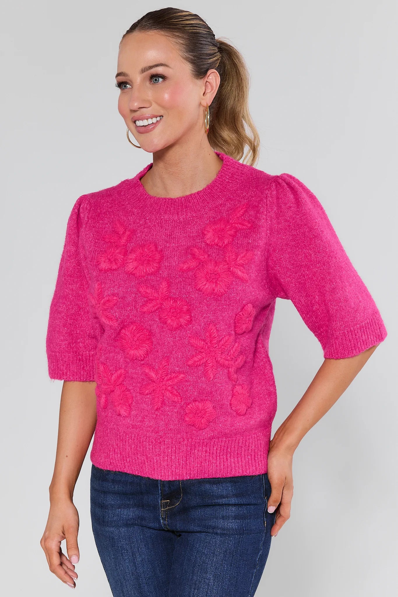 Woman wearing a pink sweater with floral patterns on a plain background