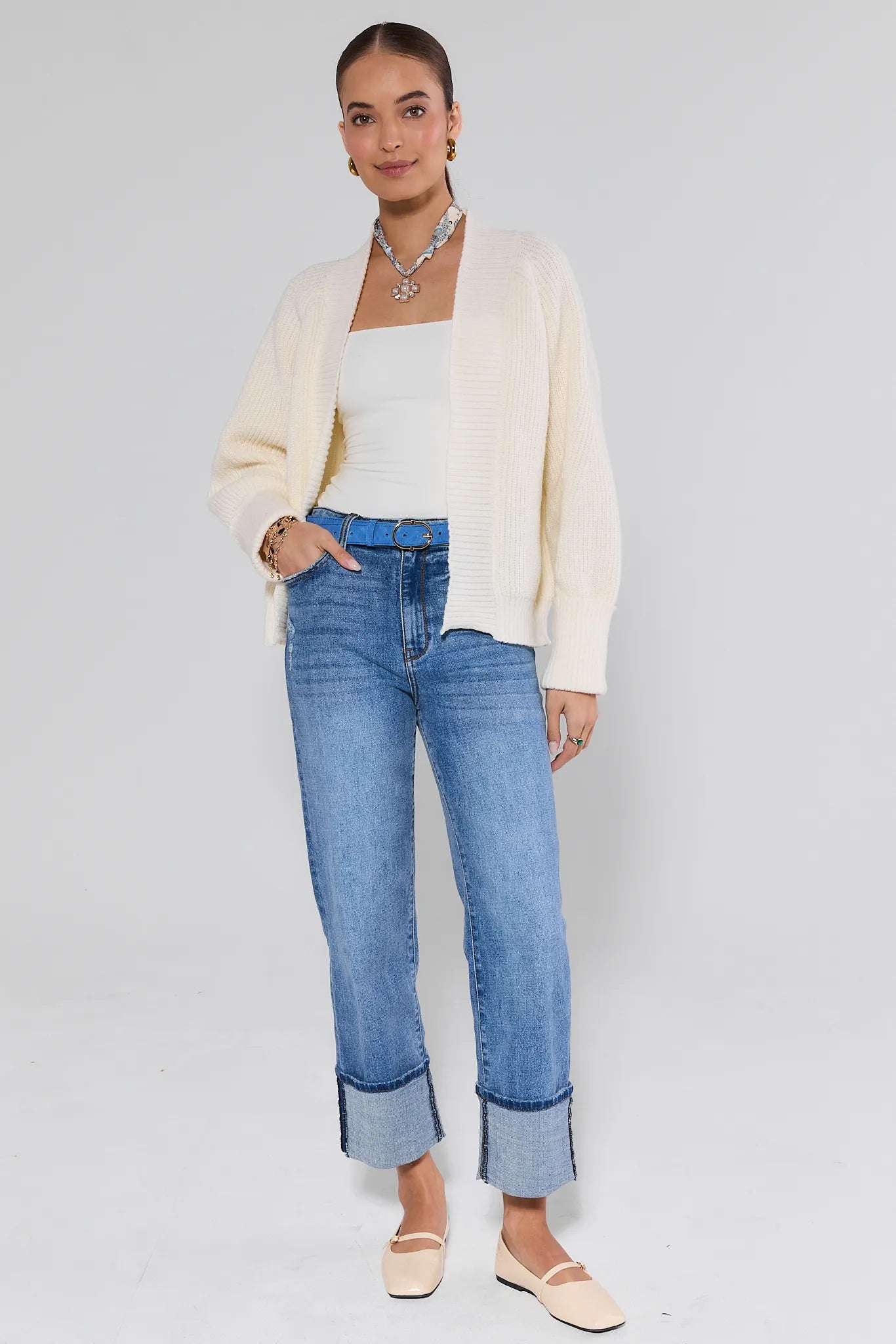 Woman wearing a cream cardigan, white top, and blue jeans on a light gray background