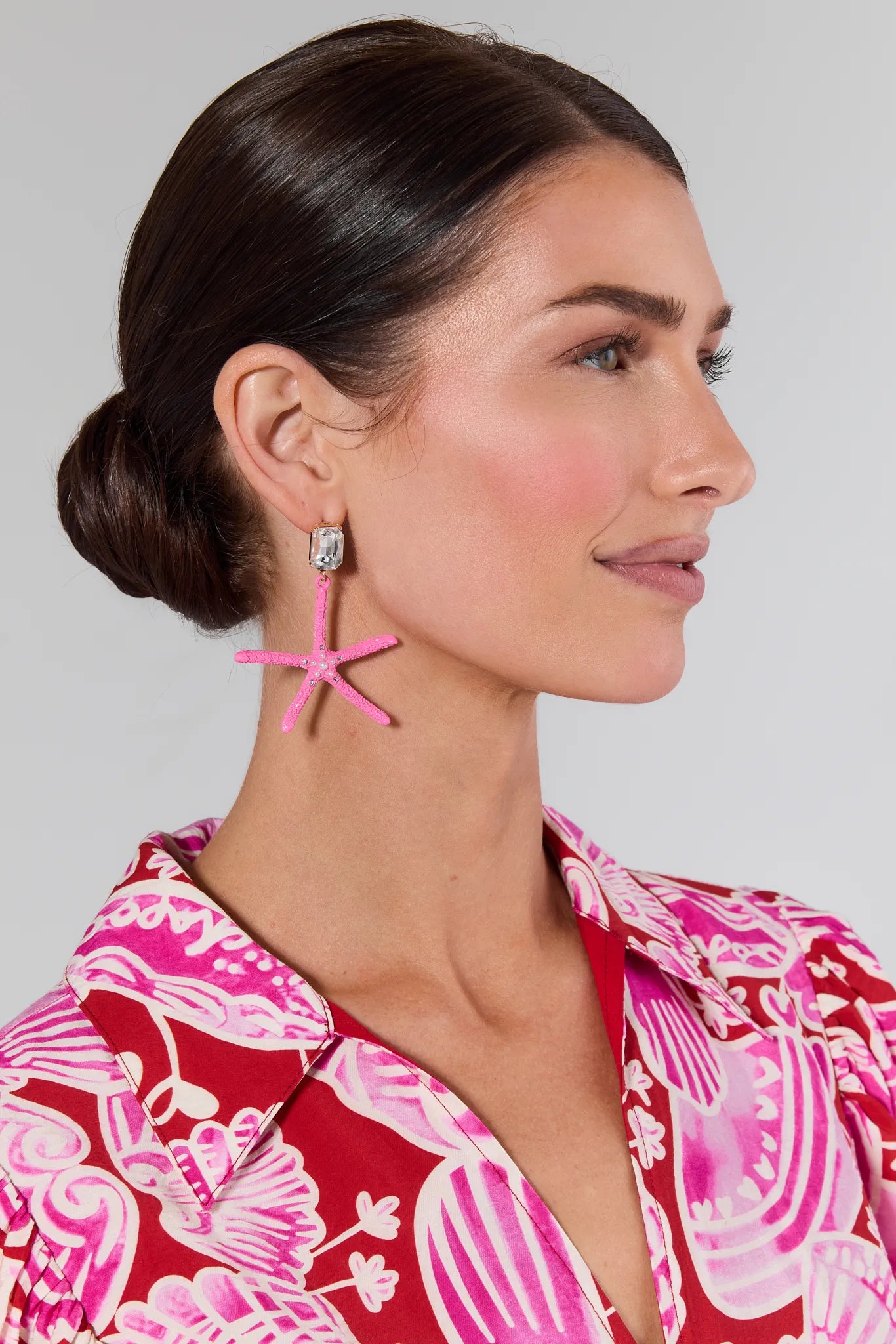 Woman wearing Cora Pink Starfish Earrings with a red and pink patterned top on a light gray background