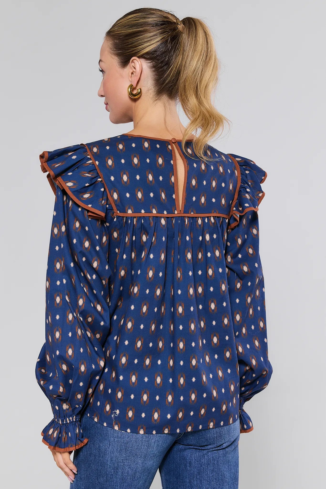 Woman wearing a blue patterned Cleo Top with brown trim on a plain background