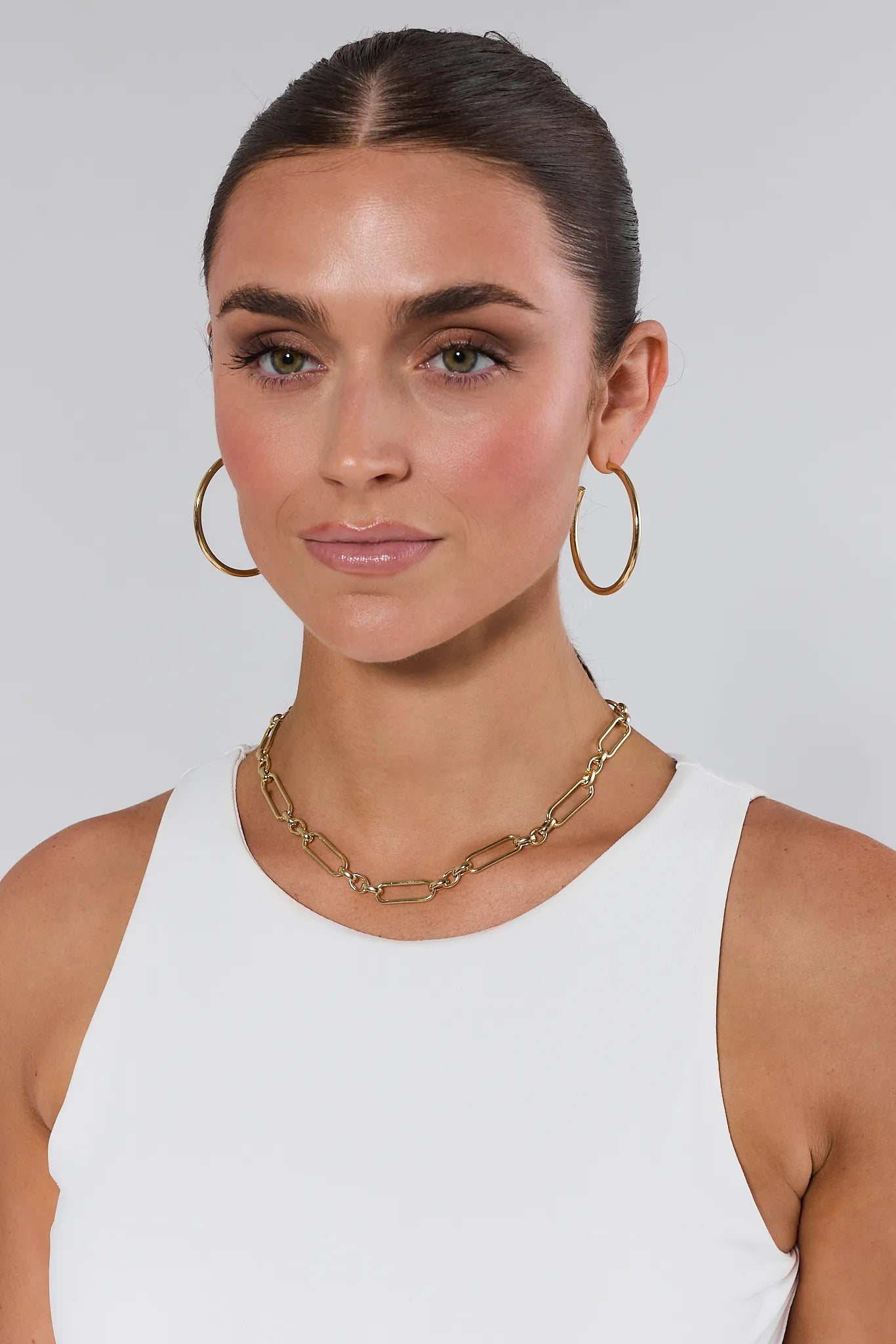 Woman wearing gold hoop earrings and a gold chain Aster Necklace against a plain background