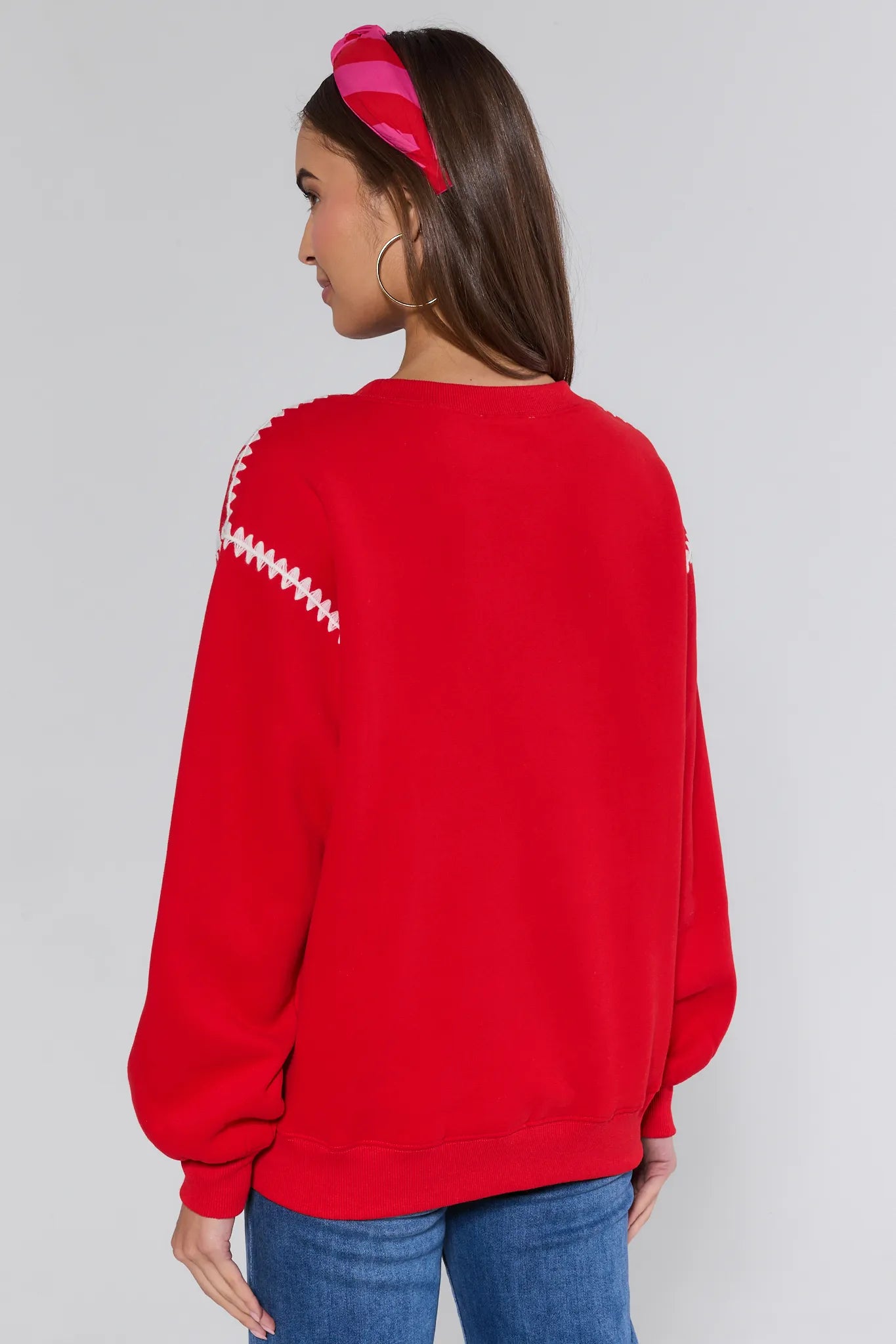 Person wearing a red sweatshirt with white patterns on the back, standing against a plain background.