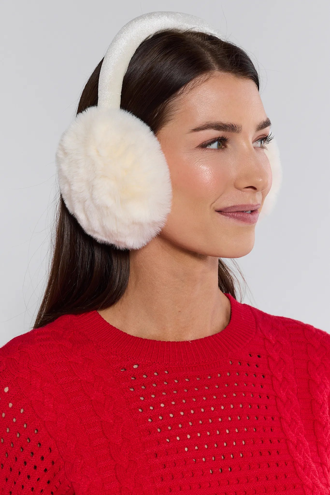Woman wearing white fur ear muffs against a plain background