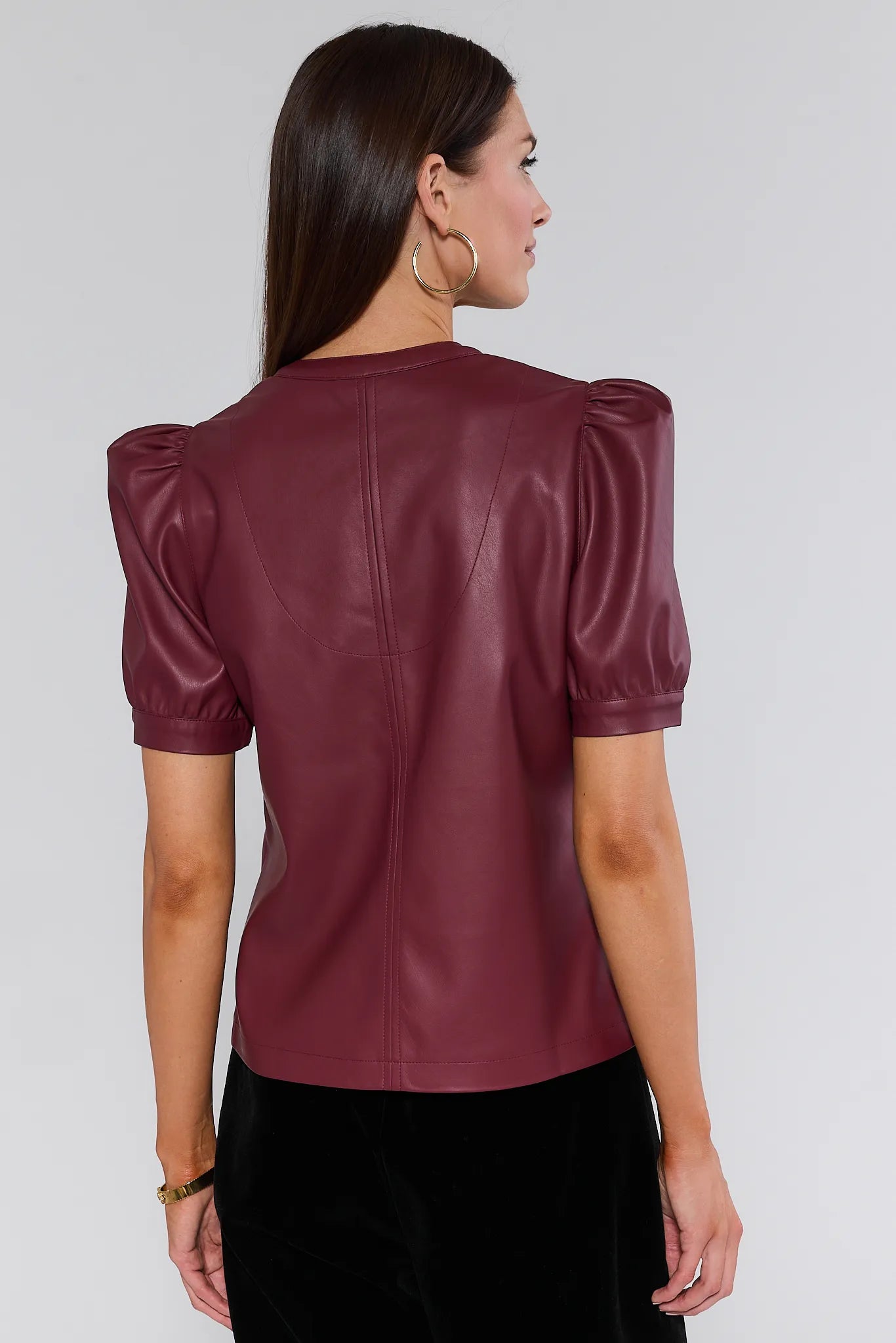 Woman wearing a burgundy leather Ariana Top with puff sleeves against a plain background