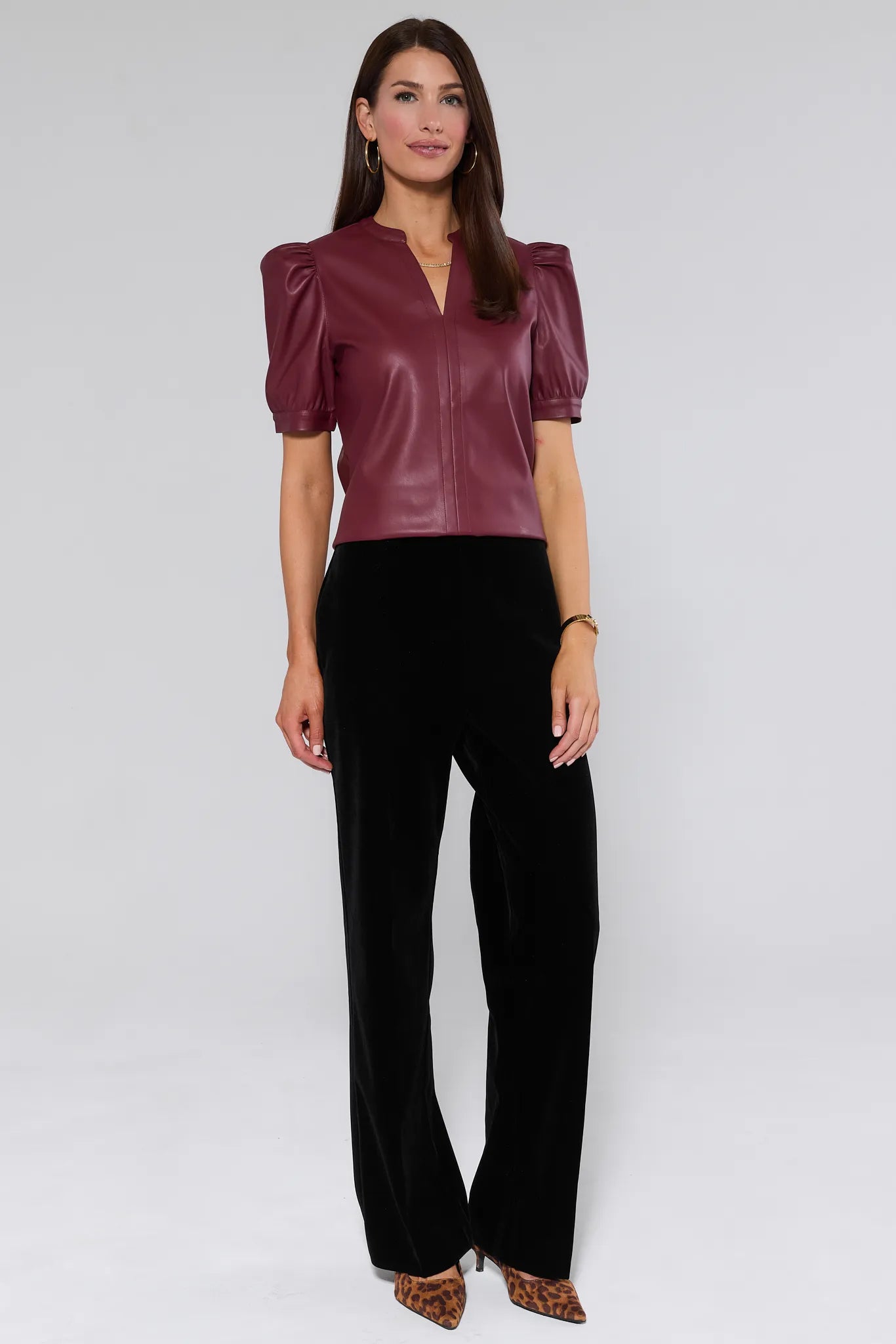 Woman wearing a burgundy leather Ariana Top with puff sleeves against a plain background