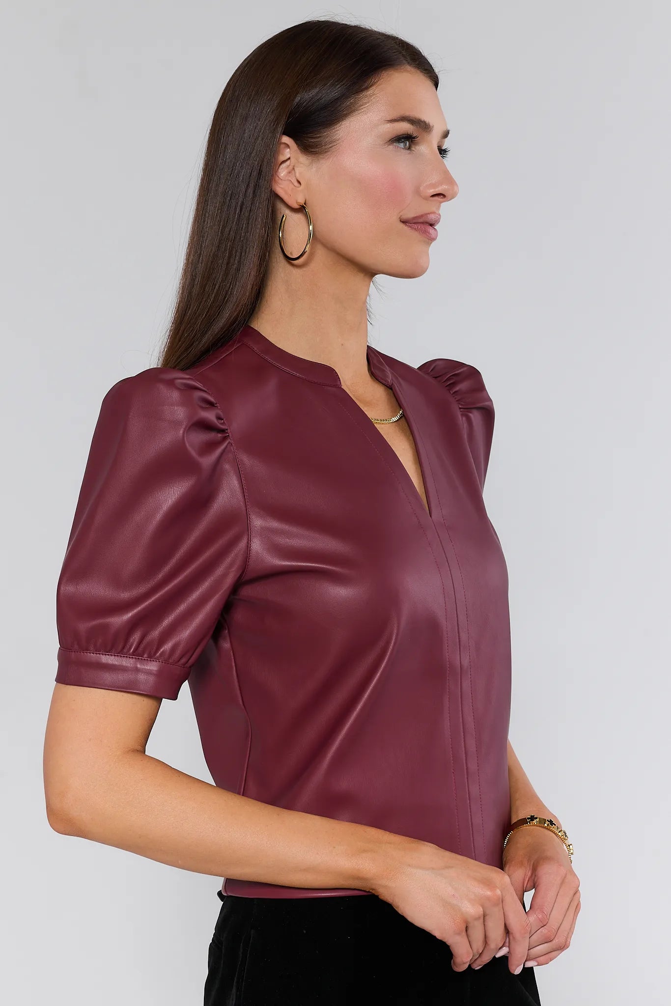 Woman wearing a burgundy leather Ariana Top with puff sleeves against a plain background