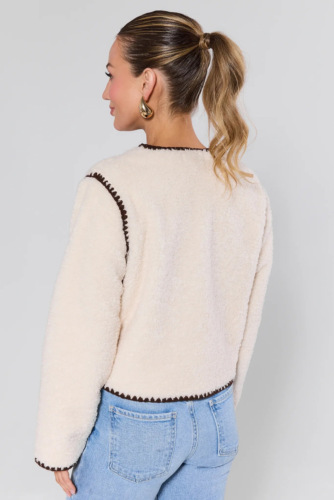 Woman wearing a Michelle Ivory Sherpa Jacket with brown trim against a plain background