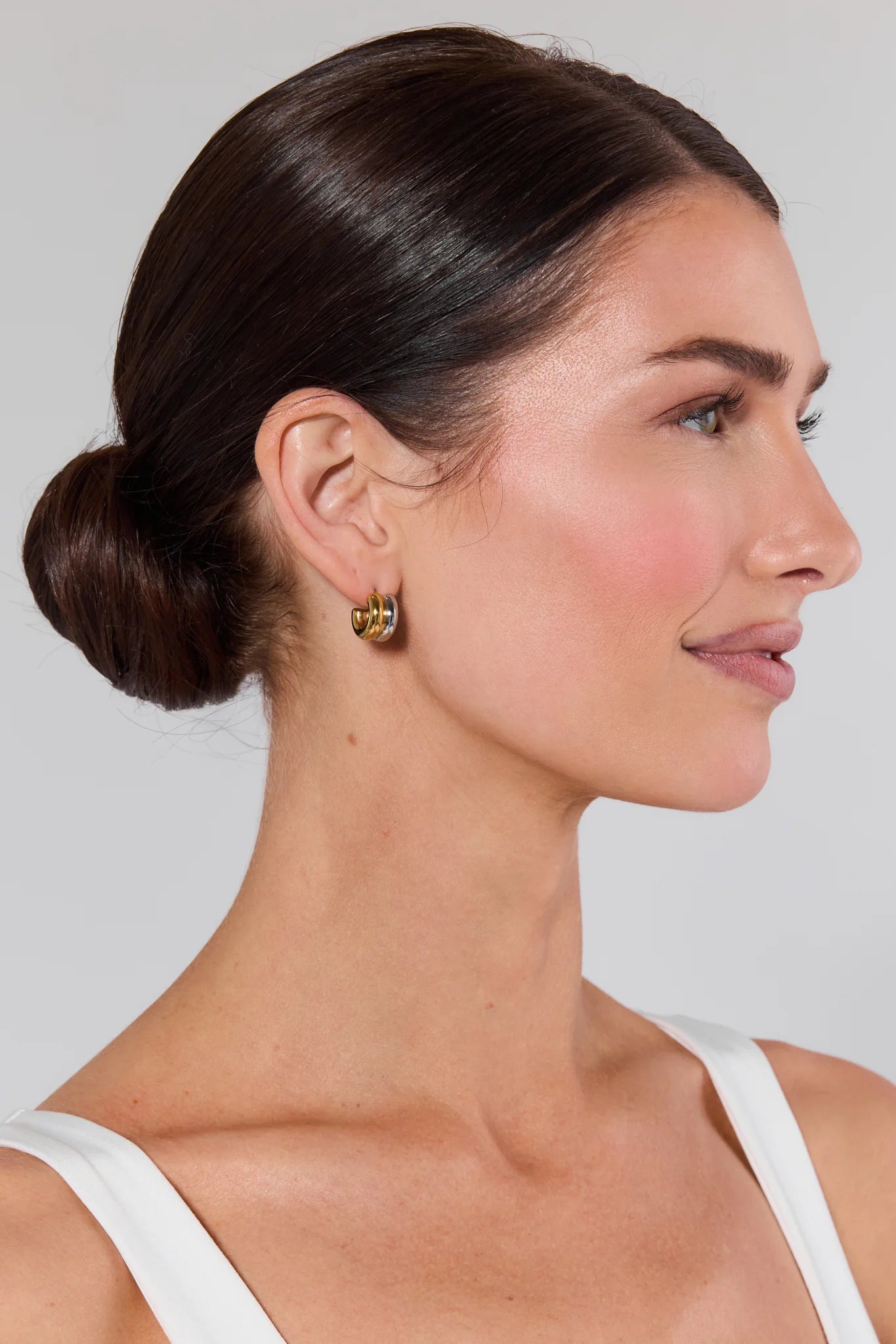 Woman with a side bun wearing gold earrings against a plain background Emma Two Toned Huggie Earrings