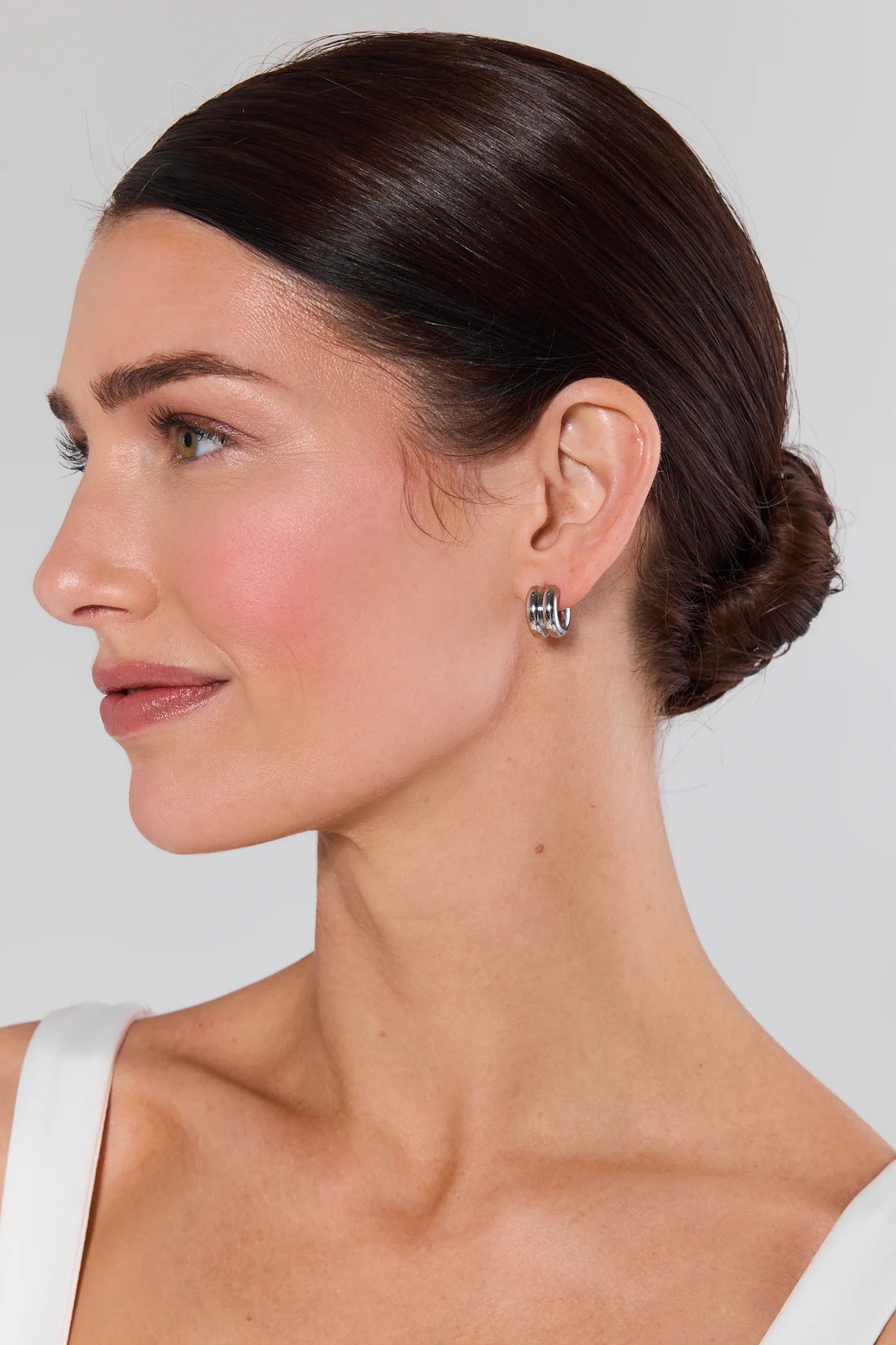 Woman wearing silver earrings with a plain background Emma Silver Huggie Earrings