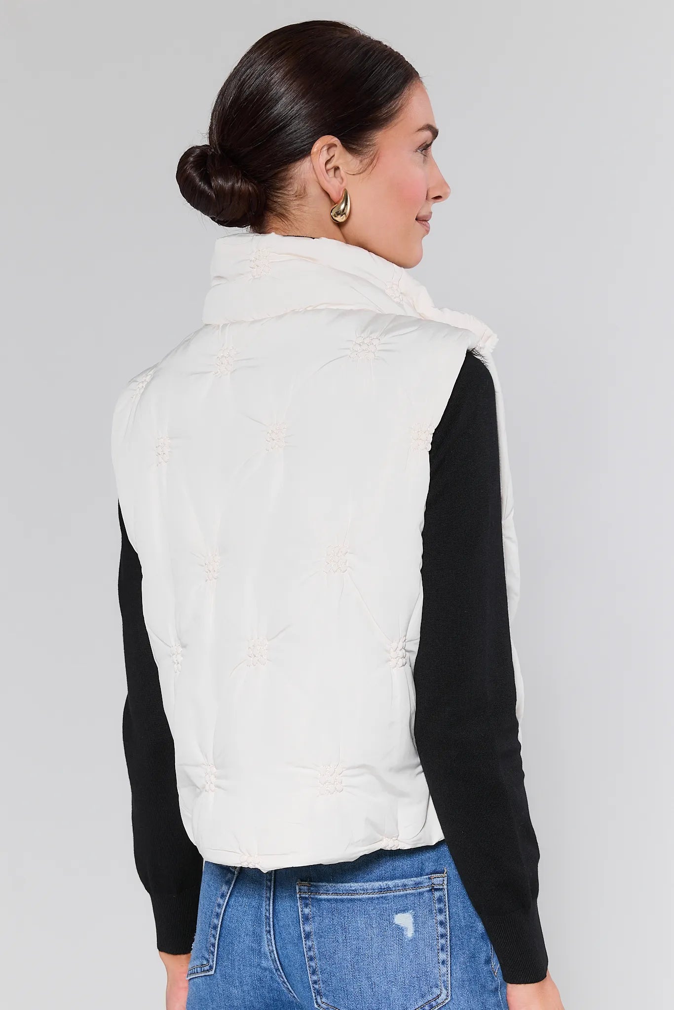 Woman wearing a Tiffany White Embroidered Puffer Vest over a black top on a gray background