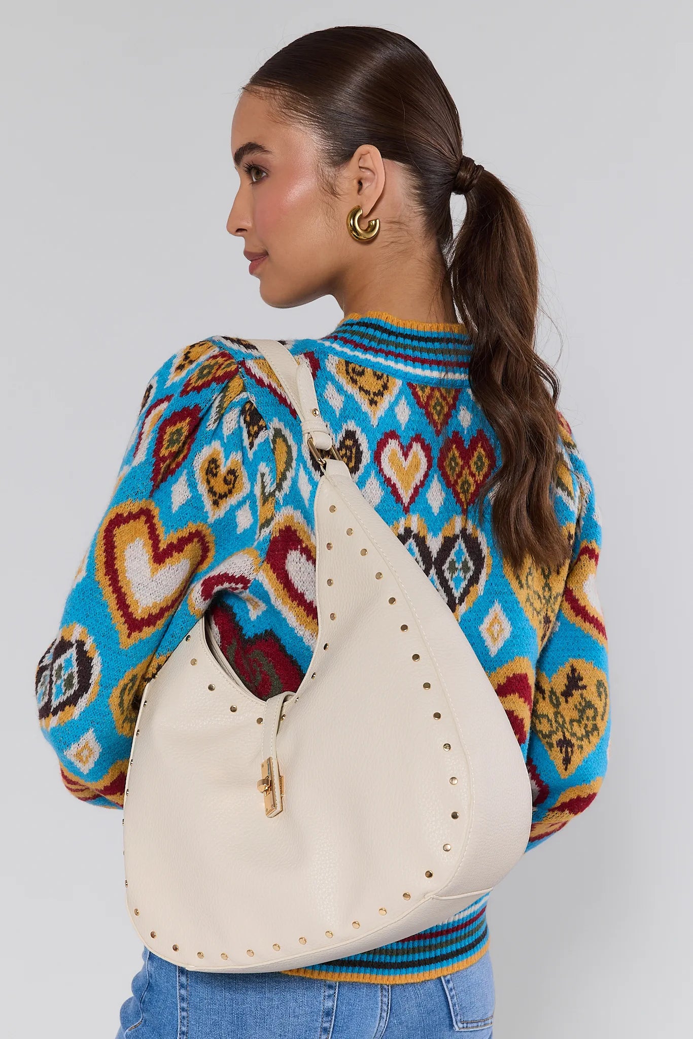 Woman wearing a colorful patterned sweater with a Olivia Cream Slouchy Shoulder Bag over her shoulder against a plain background