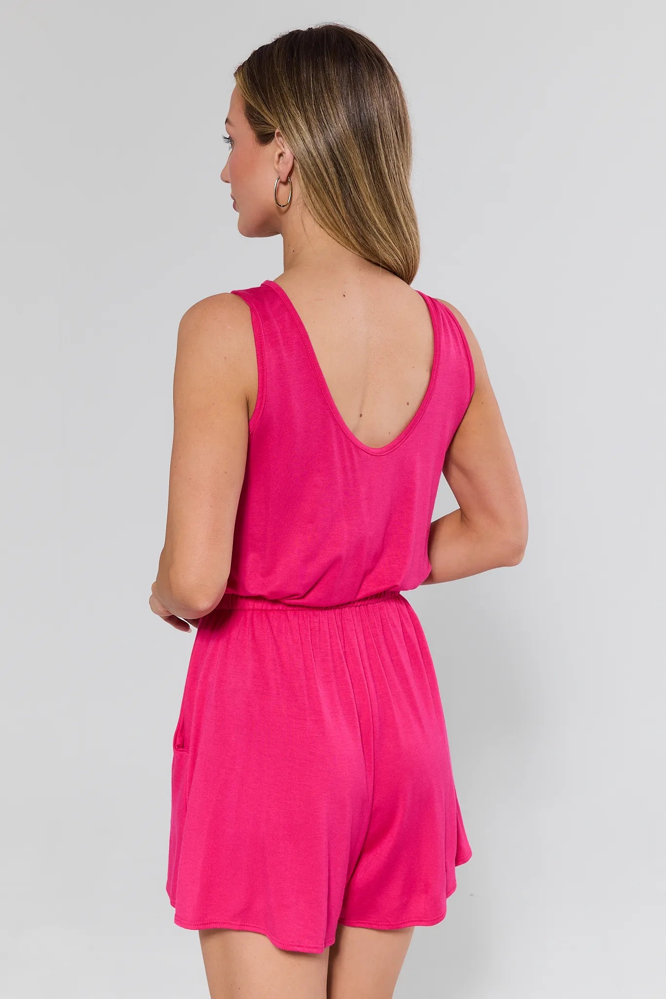 Woman wearing a bright pink romper against a plain background