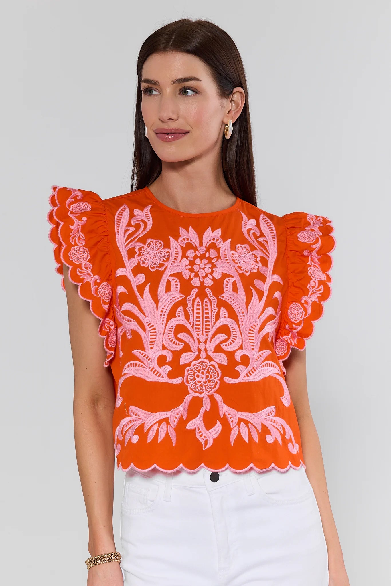 Woman wearing an orange blouse with white floral embroidery on a plain background