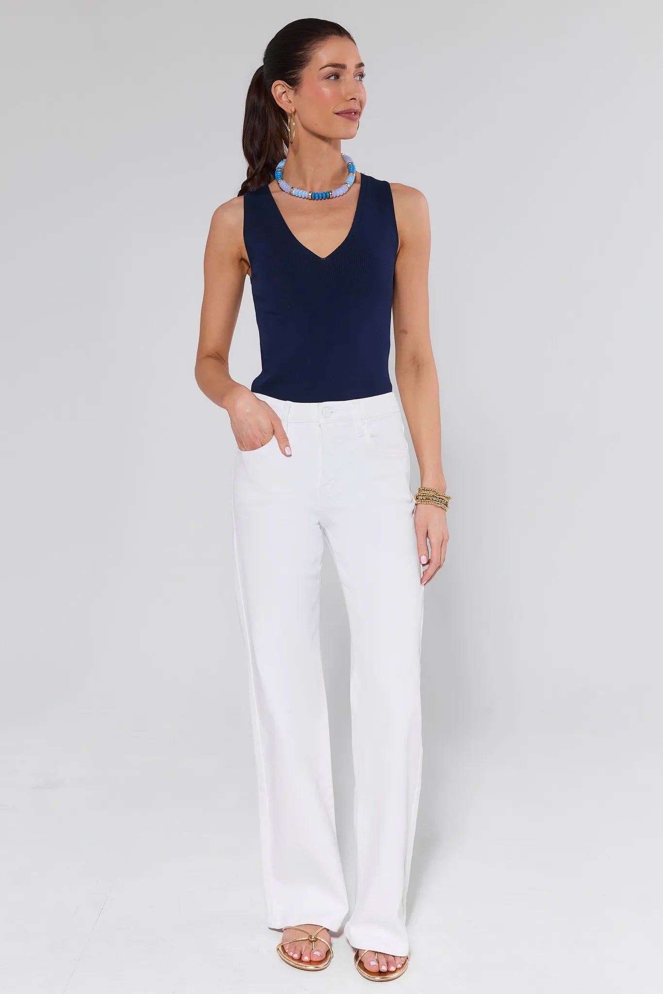 Woman wearing a navy sleeveless top and white pants on a light gray background