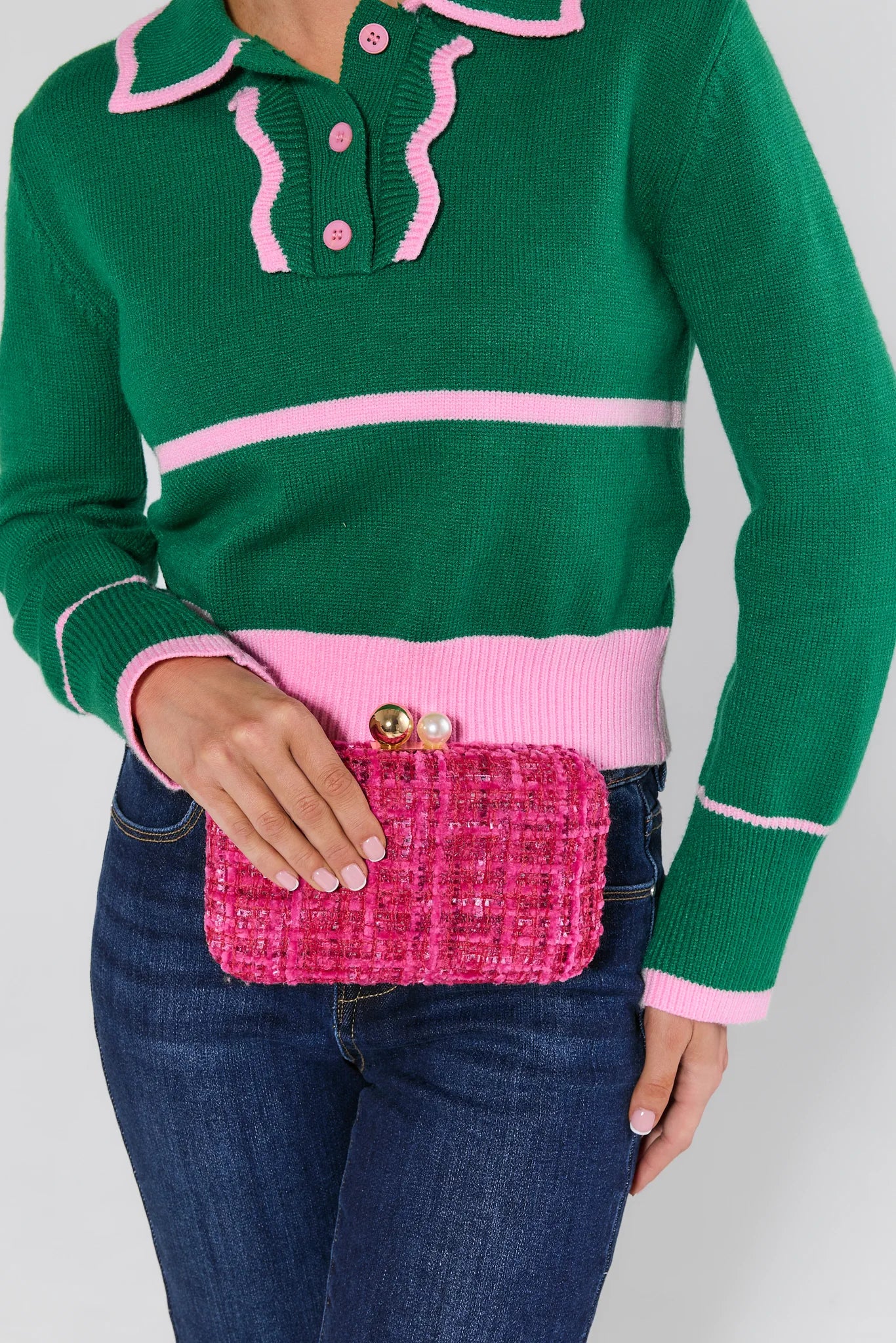 Person wearing a green sweater with pink accents, holding a pink Mabel purse against a white background