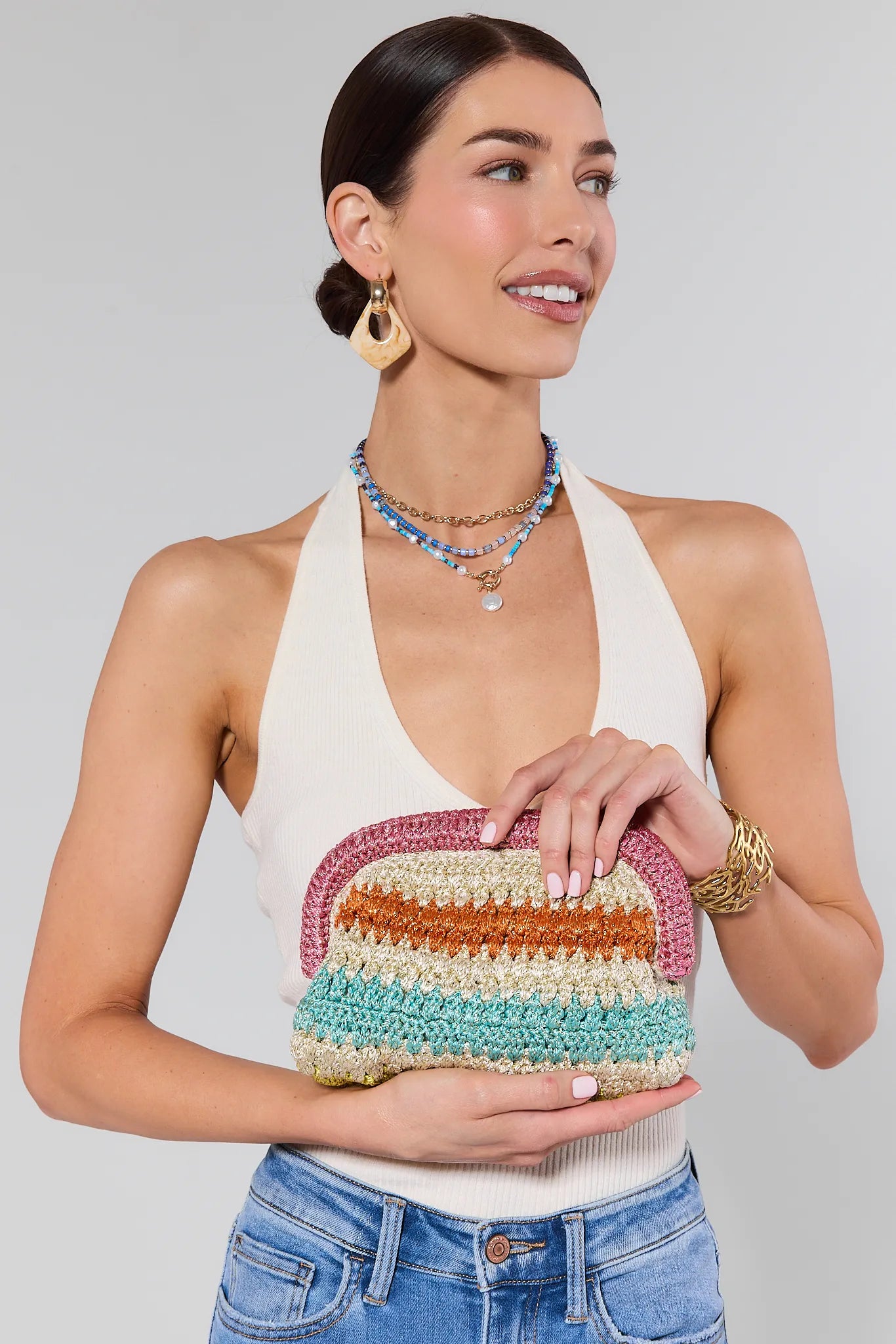 Woman holding a colorful striped clutch against a plain background