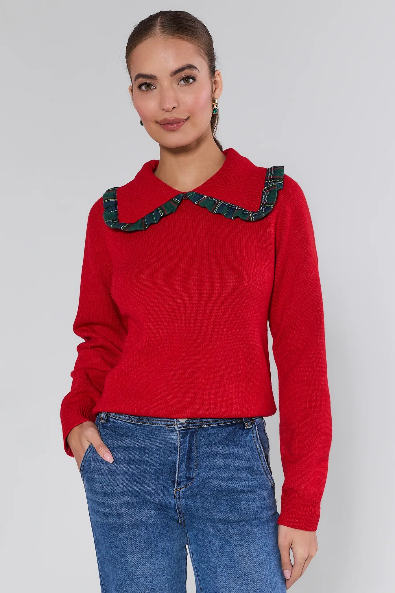 Woman wearing a red sweater with green trim against a plain background