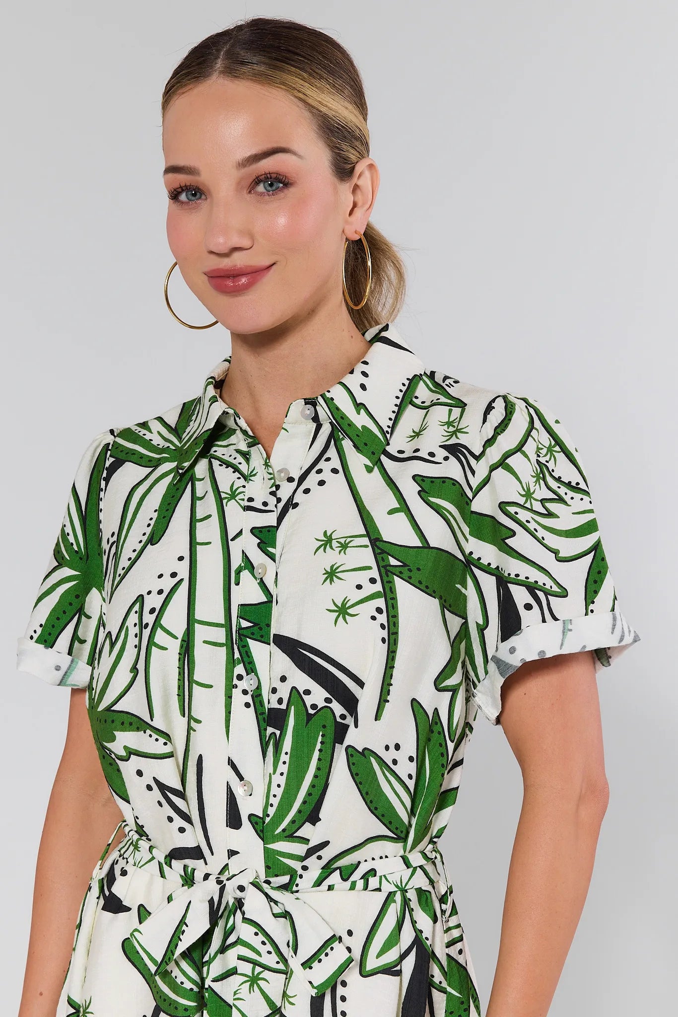 Woman wearing a white dress with green leaf pattern against a plain background