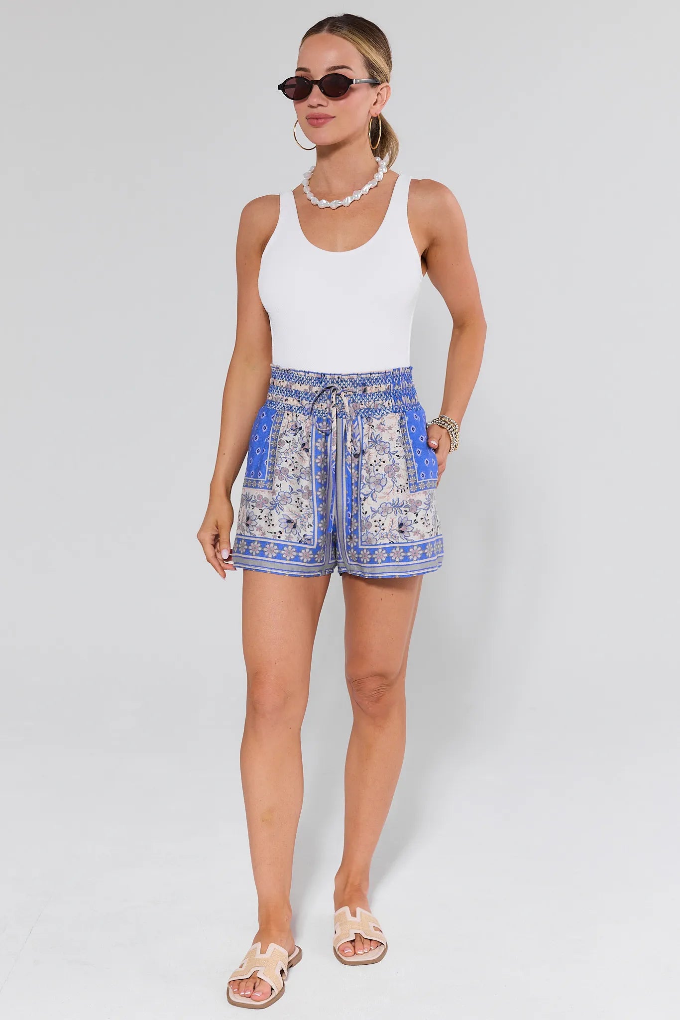 Woman wearing a white tank top and blue patterned shorts on a plain background
