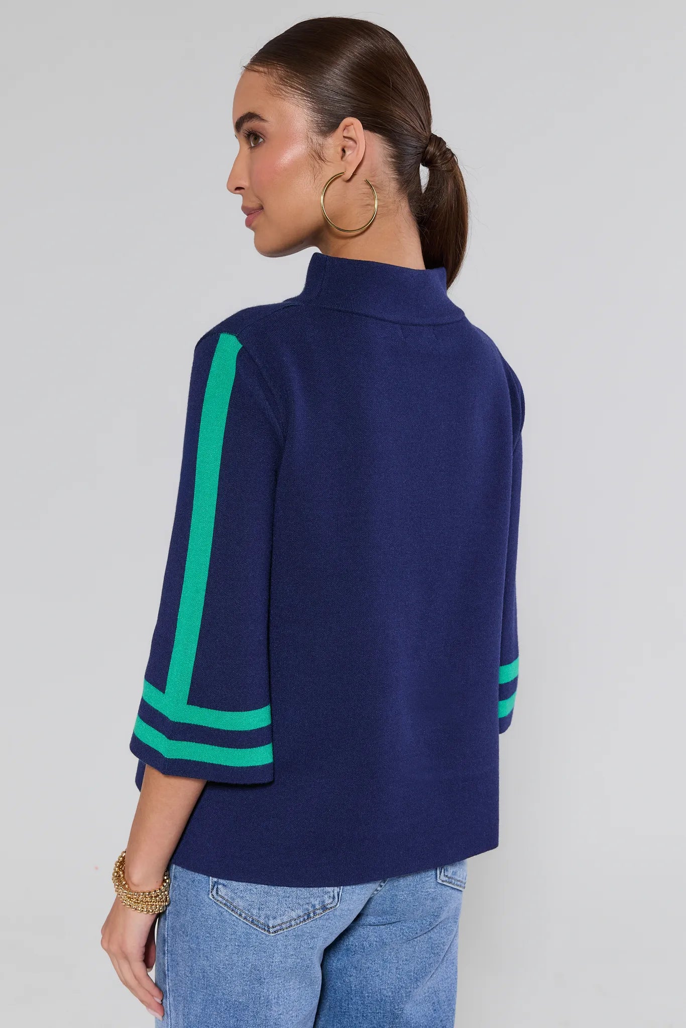 Woman wearing a navy blue jackie sweater with green on a gray background