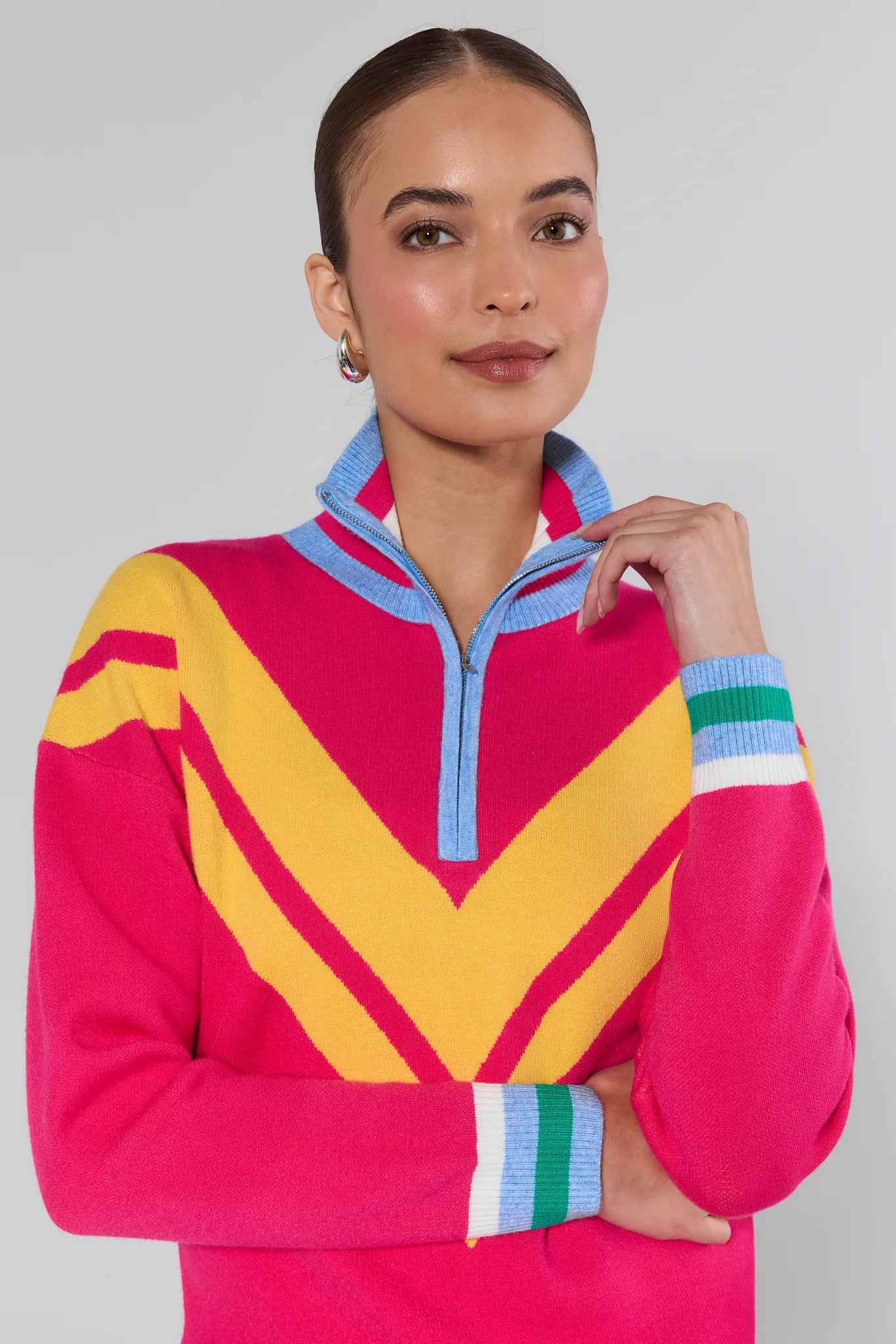 Woman wearing a colorful sweater with a pink base and yellow and blue accents on a gray background