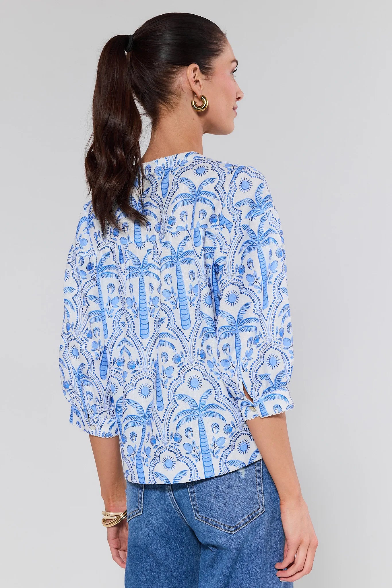 Woman wearing a blue and white patterned blouse with blue jeans on a gray background