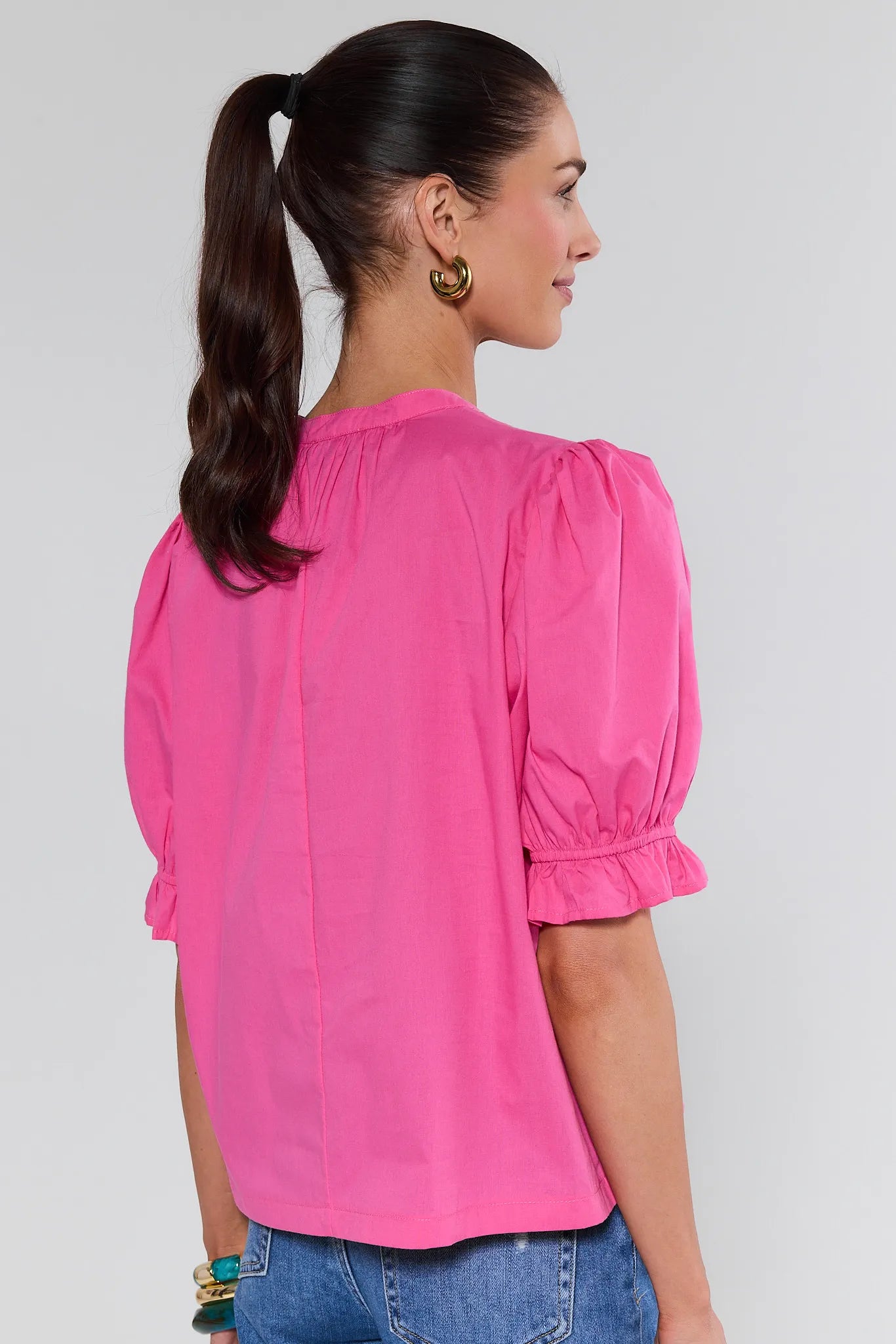Woman wearing a bright pink blouse with puffed sleeves on a plain background