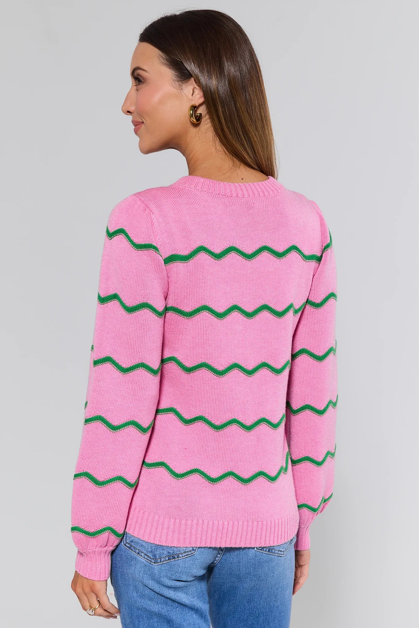 Woman wearing a pink sweater with green zigzag pattern on a gray background