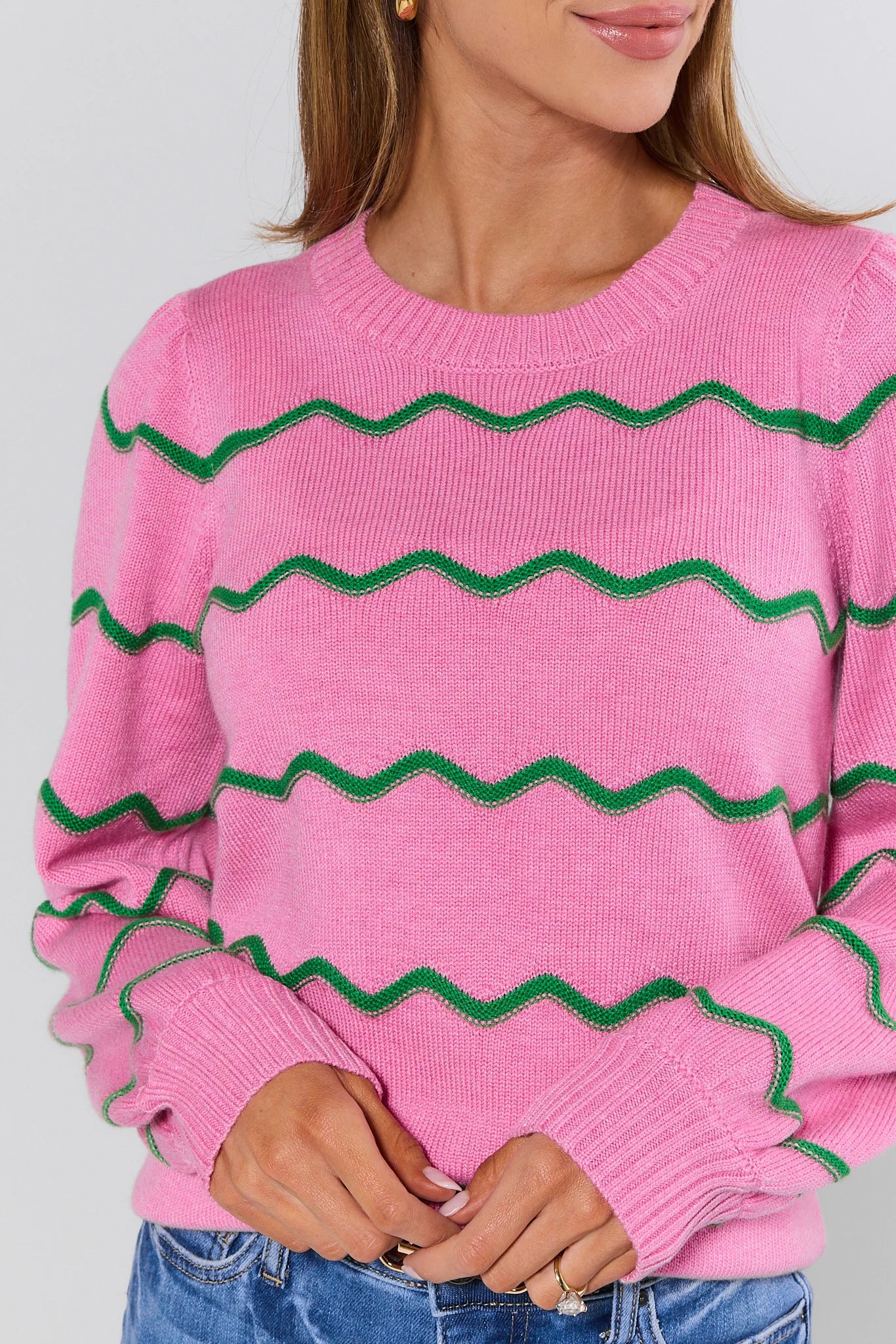 Person wearing a pink sweater with green zigzag patterns on a plain background