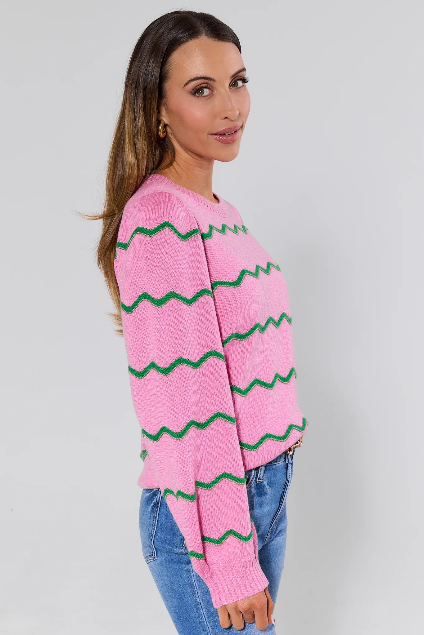 Woman wearing a pink sweater with green zigzag pattern on a plain background